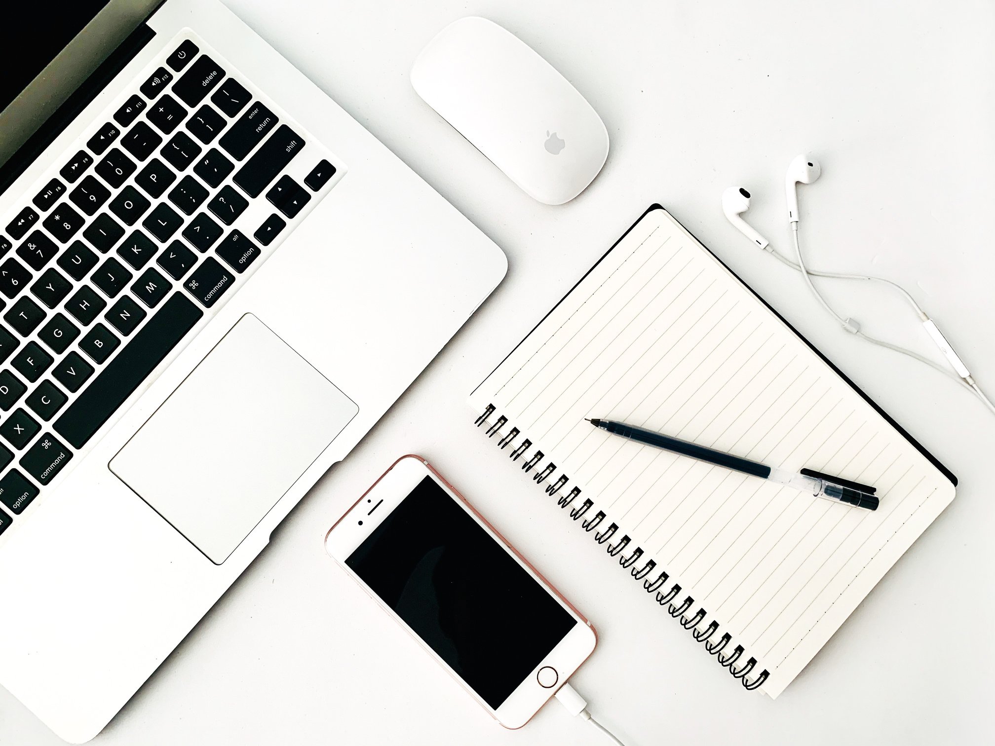 Laptop with smartphone and notebook near earbuds on table